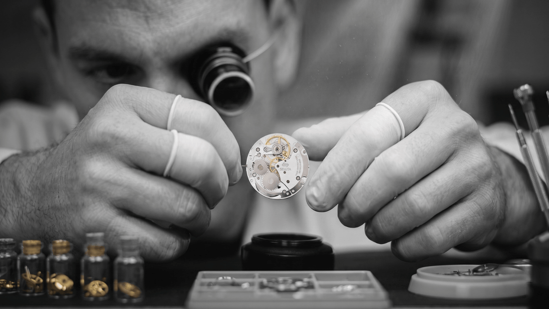 A watchmaker closely examines an intricate sellita sw210 1, the sellita watch movement, using a jeweler's loupe at his workbench.