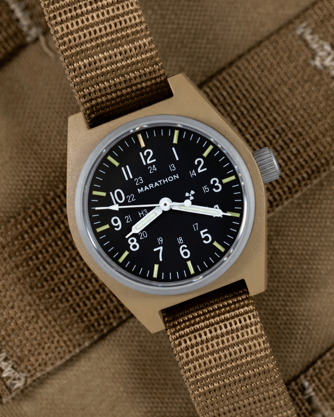 Marathon Desert Tan GPM on a ballistic nylon strap against tactical gear. Field Mechanical, Type II watch designed for rugged ground operations.