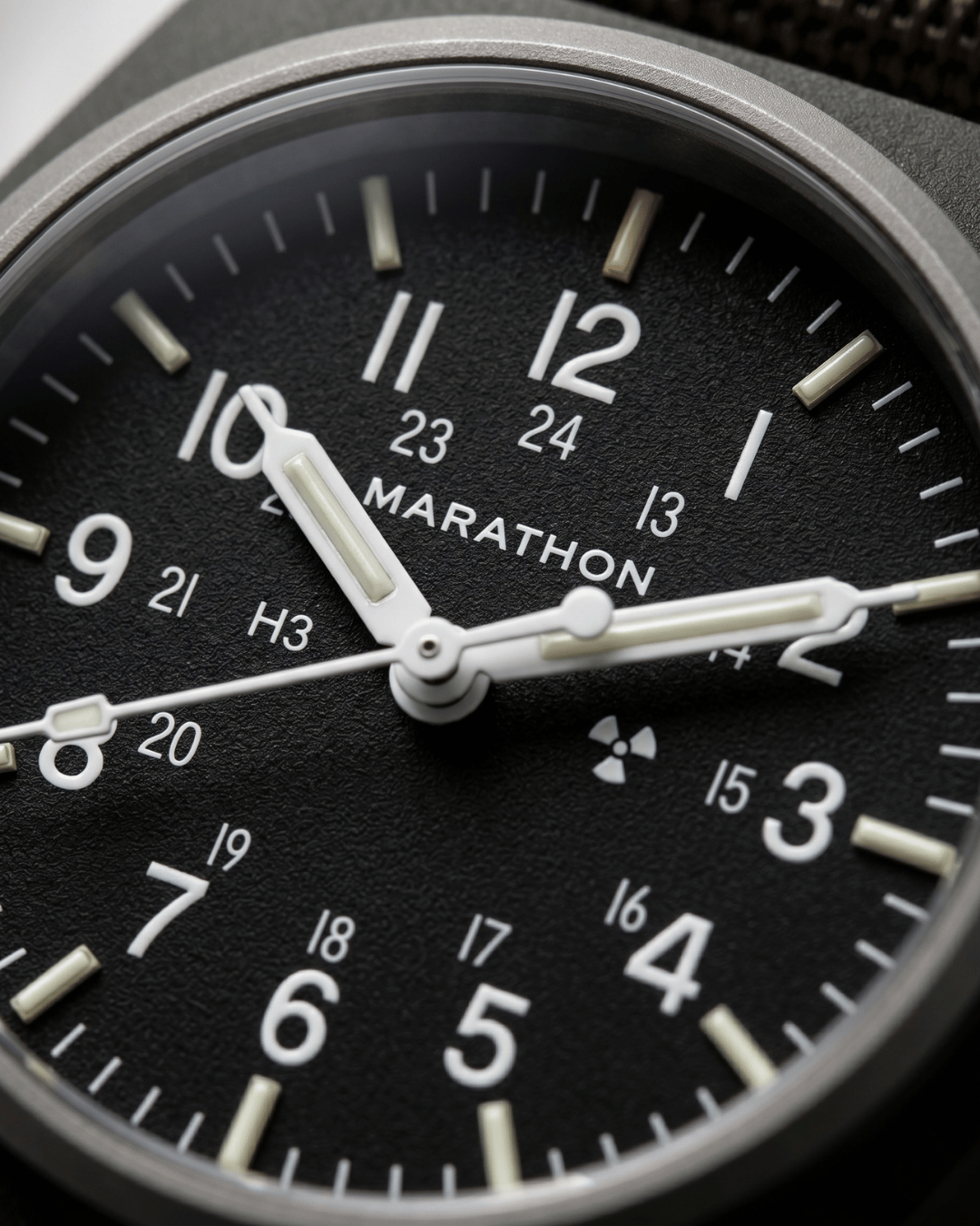 Close-up of the Marathon GPM Sage Green dial. Features Tritium gas tubes for visibility and a scratch-resistant sapphire crystal. Professional military watch.